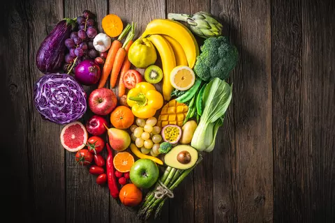 Verschiedene frische Früchte und Gemüse, die in Herzform auf einem rustikalen Holztisch arrangiert sind, und die Vielfalt und Bedeutung gesunder Ernährung darstellen.